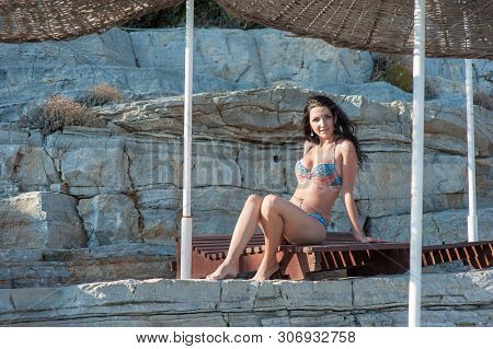 A Beautiful Brunette Sits On A Lounger. Young Girl In Sexy Bikini