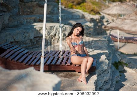A Beautiful Brunette Sits On A Lounger. Young Girl In Sexy Bikini