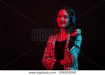 Cheerful Young Girl Wearing Heaphones And Smiling To The Camera In Studio With Colored Lighting