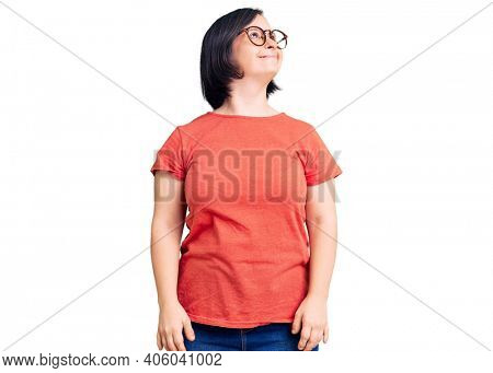 Brunette woman with down syndrome wearing casual clothes and glasses looking away to side with smile on face, natural expression. laughing confident. 