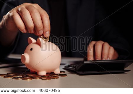 Businessman Is Counting Profit On A Calculator In Office, Piggy Bank With Coins At Desk. Economy And