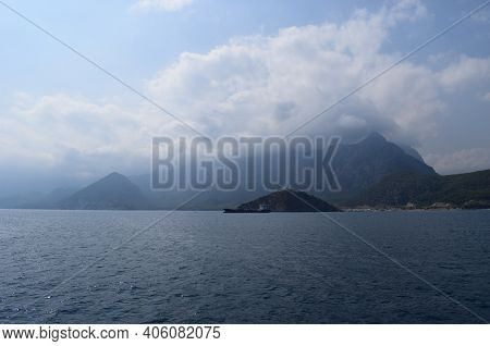 Cargo Ship Sailing By The Coast Against Cloudy Blue Sky And Rippled Sea Near The Turtle Island, Anta