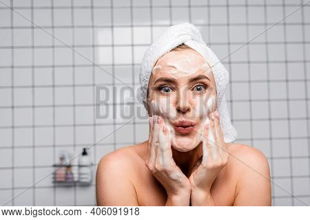 Surprised Woman With Naked Shoulders Applying Foam Cleanser In Bathroom