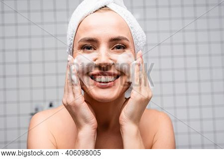 Happy Woman With Naked Shoulders Applying Foam Cleanser In Bathroom