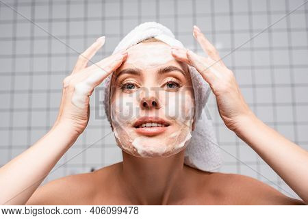 Woman With Naked Shoulders Applying Foam Cleanser In Bathroom