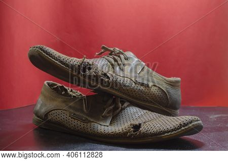 Old Torn Yellow Summer Shoes On A Red And Black Background. Two Men's Heavily Worn Leather Shoes. Se