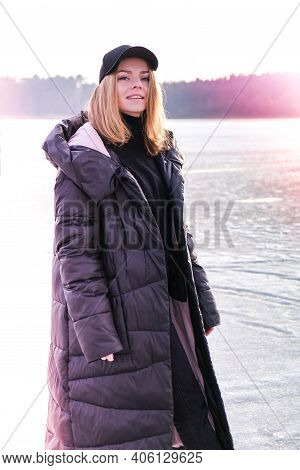 Young Female Smiling And Looking At A Camera In A Snow Landscape. Happy Hipster Girl With Hip Hop Wa