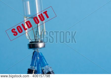 A Close-up Medicine Ampoule, Upside Down, And Five Medical Needles Stuck In The Bottle Cap On A Blue