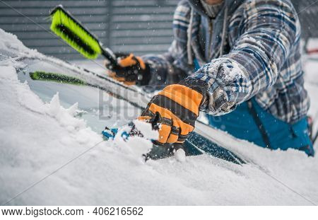 Caucasian Driver Removing Snow And Ice From His Car Windshield. Extreme Winter Season Weather And Th