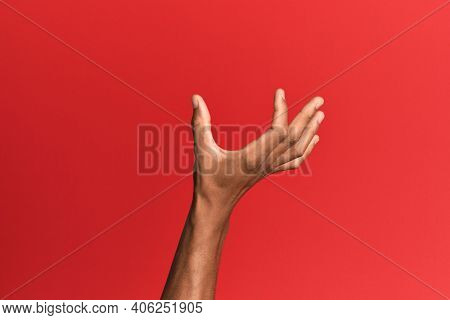 Hand of hispanic man over red isolated background picking and taking invisible thing, holding object with fingers showing space 