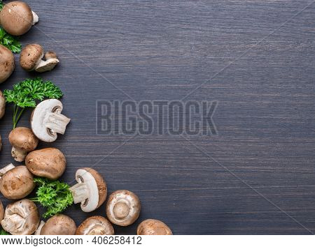 Brown colored edible mushrooms or cremini mushrooms on black table with herbs. Top view.