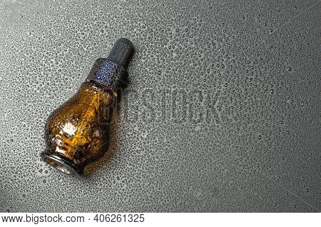 Bottle With Natural Body Oil On A Black Background With Drops Of Foda. Serum In A Glass Bottle. Cosm