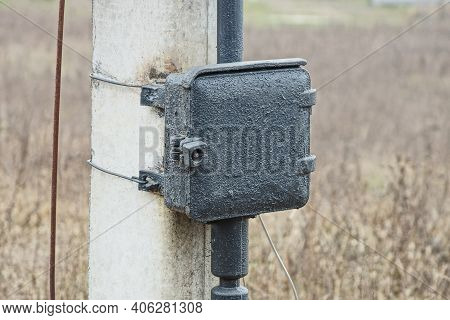 One Black Old Iron Square Box For Electrical Wires On A Gray Concrete Pillar Outside