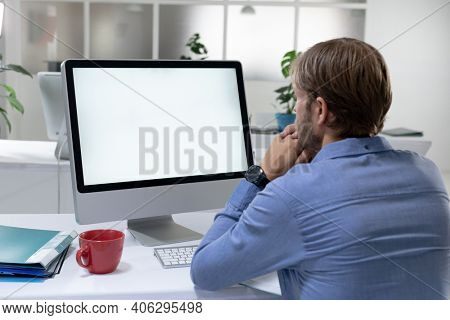 Rear view of caucasian businessman sitting at desk making video call using desktop computer. working online, social distancing during quarantine lockdown.