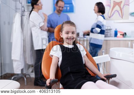 Little Girl In Dendistiry Office Showing Milk Tooth While Parent Is Discussing With Dentist Doctor. 