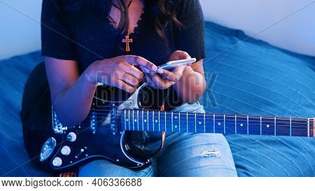 Young Woman Musician Holding Acoustic Guitar While Using Smartphone. Close Up. High Quality Photo