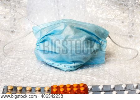 A Metaphor Of A Face In A Blue Medical Mask Looks At Blisters Of Different Pills. Virus And Pandemic