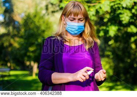 Mature Middle-aged Woman In Blue Medical Mask, Violet Blouse Washes Hands With A Gel Antiseptic Spra