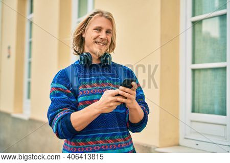 Young scandinavian student man smiling happy using smartphone and headphones at the city.