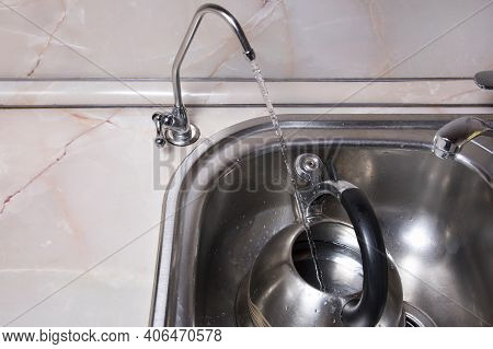 Pouring Filtered Water Into Kettle From Water Filter. Closeup Of Sink And Faucet. Drinkable Water In