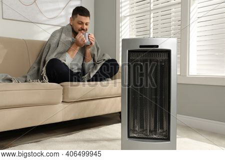 Man With Cup Of Hot Drink In Living Room, Focus On Electric Ultrared Heater