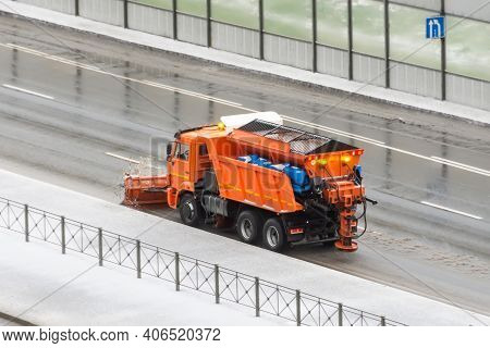 Snowplow Gritter Is Driving On The Side Of A Road Covered With A Thin Layer Of Ice