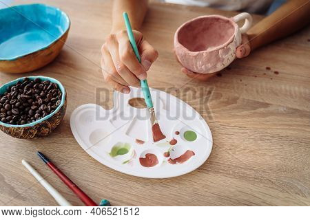 Hand Dipping Paintbrush Into Palette On Wooden Table. Finishing Manufacturing Procces Of Clay Potter