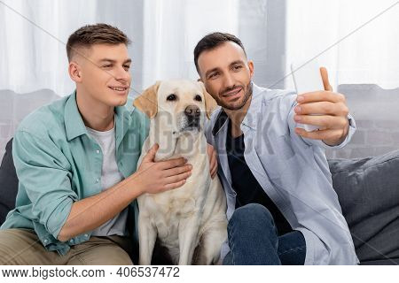 Cheerful Same Sex Couple Smiling And Taking Selfie With Labrador.
