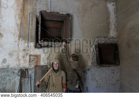 Boys Standing In An Abandoned Building. Wandering Boy. Man In A Protective Cloak With A Hood. Post A