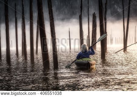 Adventurous Girl Kayaking On An Infatable Kayak In A Beautiful Lake. Dark Dramatic Art Render. Taken