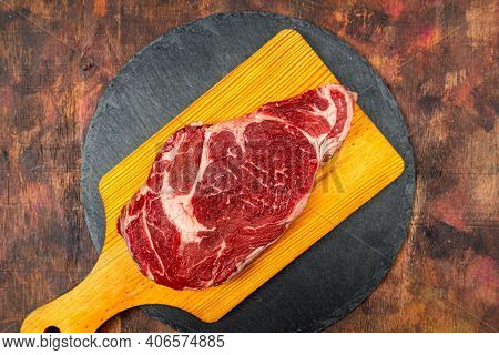 Raw Beef Ribeye On A Round Slate Plate On An Old Wooden Table In Brown Tones. Gourmet Food Concept