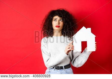 Real Estate. Sad Woman Thinking Of Buying Own House, Showing Paper Home Cutout And Looking Up With U