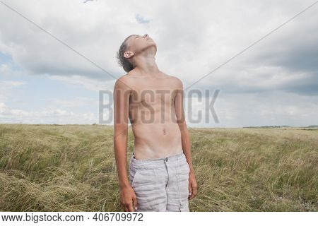 Boy In Shorts Stands In The Field. Boy Looks To The Sky. Dreamer Guy