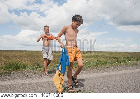 Two Boys In Shorts Cross The Road In The Countryside.
