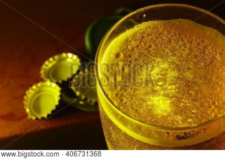 Glass Of Beer Seen Up Close With Beer Bottle Caps And A Corkscrew.
