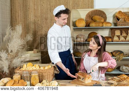A New Clerk Learns To Cut The Bread Properly Under The Bakers Supervision. An Attractive Saleswoman 