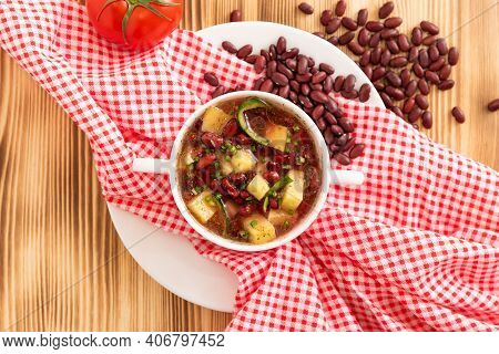 Traditional Bean Soup With Vegetables And Potatoes On A Wooden Background With Garlic.