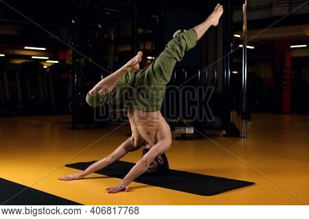 A Young Yogi With A Bare Torso Performs A Complex Element Of Yoga Is Shirshasan. Yoga Trainer Stands