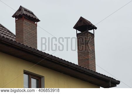 Two Brown Brick Chimneys On The Roof Of A Private House Against A Gray Sky