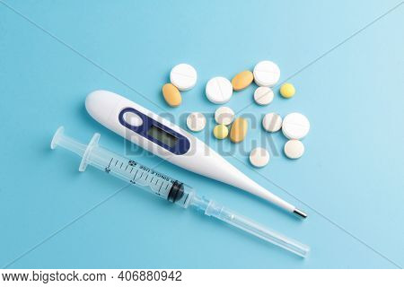 Medical White, Gray, Yellow Tablets, Injection Syringe And Thermometer On A Blue Medical Background.