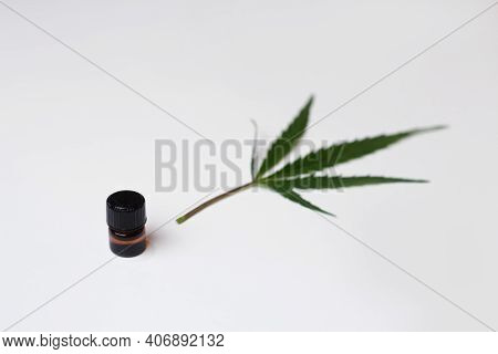 Cannabis Oil. Marijuana Oil In A Bottle With A Cap. Blurred Marijuana Medicinal Cannabis Leaf On Whi