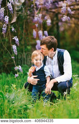 Father Is Kissing His Baby Boy On Top Of The Head With A Wysteria Blooming In The Background