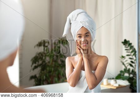 Satisfied Millennial African American Woman In Towel Presses Hands To Face And Looks At Reflection I