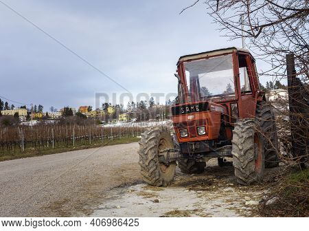 Old Tractor With A Snowy Mountain Village In The Background, Spiazzi In The Province Of Verona