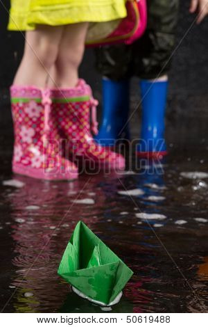Green paper boat on the background of children feet wearing in colorful rubber boots