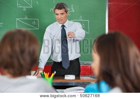 Angry male teacher pointing at students in classroom