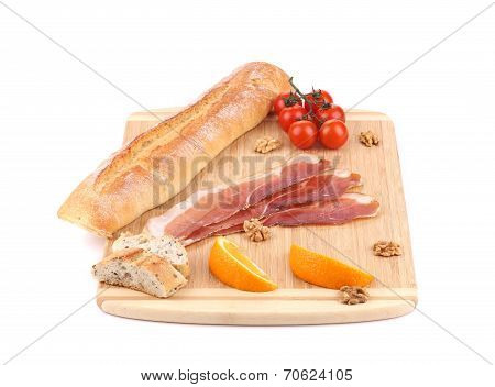 Prosciutto and tomatoes on cutting board.