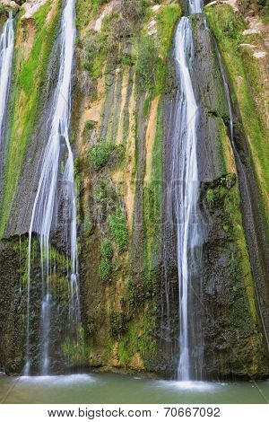 Three parallel streams of water running down the steep slope and fall in oval pool. Three-jet scenic waterfall in the mountains
