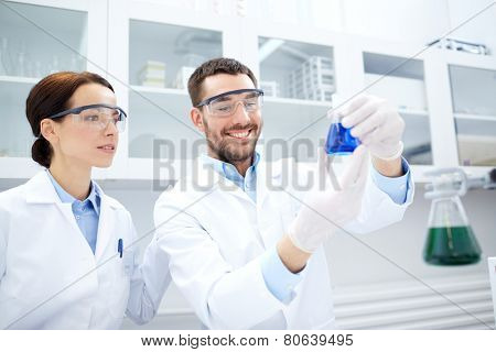 science, chemistry, technology, biology and people concept - young scientists holding flask with reagents and making test or research in clinical laboratory