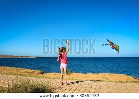 A little girl runs into the sky flying snake by the sea